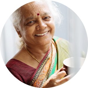 Woman with a bindi holds a mug and smiles at camera